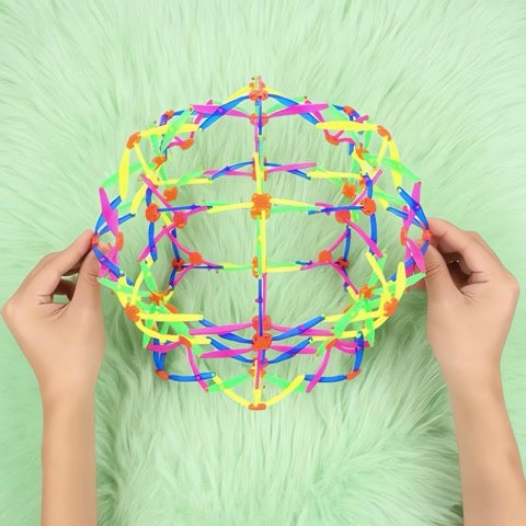 Colorful geometric structure made of interlocking sticks held by hands on a green background