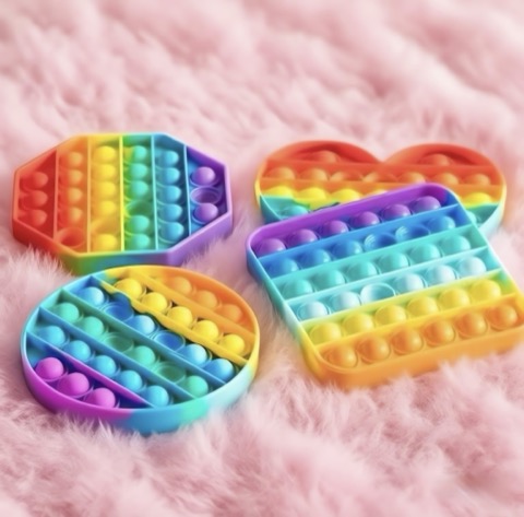 Four rainbow-colored pop-it fidget toys on a pink fluffy surface