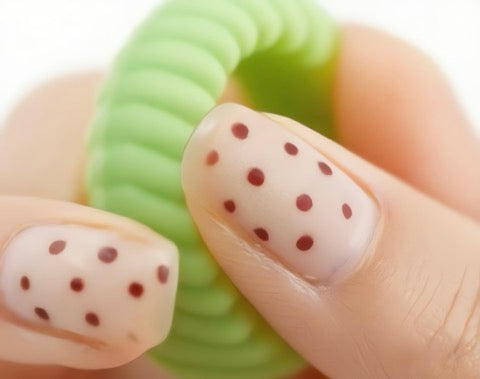 Close-up of a hand with polka dot nail design holding a green object.