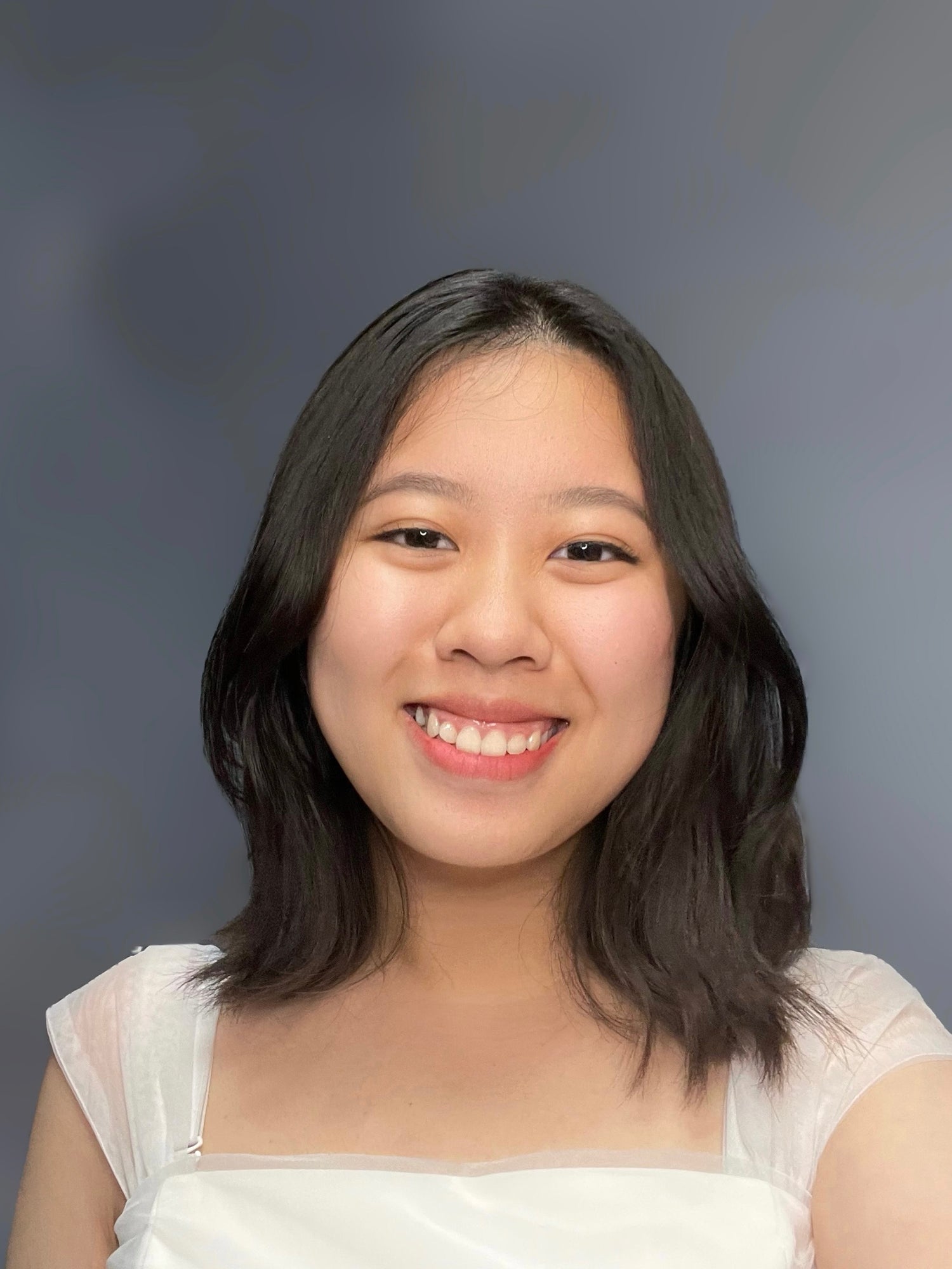 Woman with shoulder-length dark hair wearing a white top against a gray background