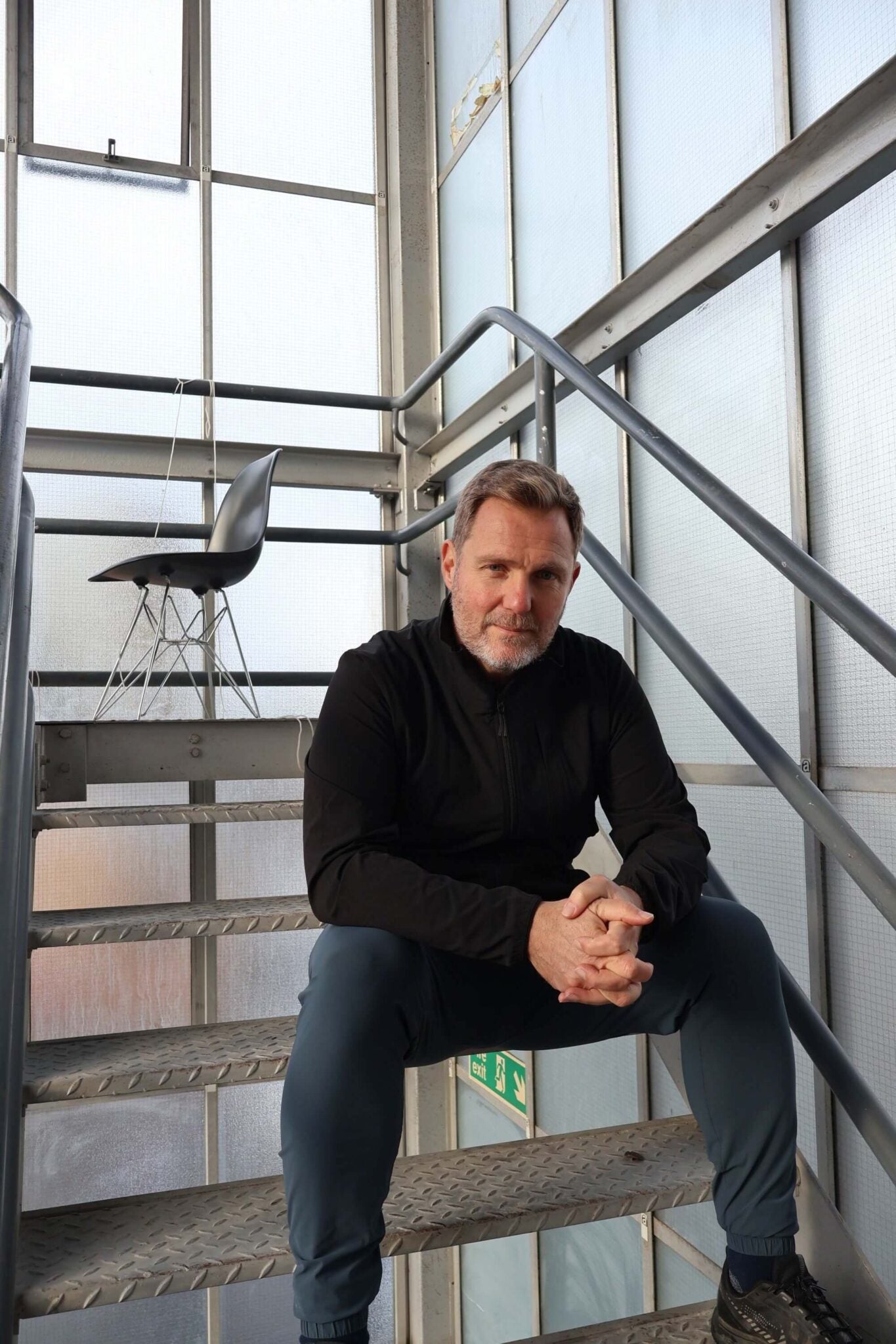 Simon Squibb sitting on a staircase in a modern building with large windows