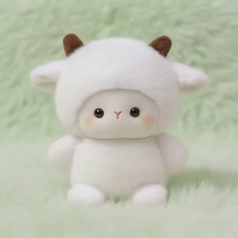 A short, static video of a fluffy white plush lamb. It is wearing a white hood with two small brown horns, and it has large, dark eyes and a sweet, loving expression. The plushie is sitting on a soft, mint-green fluffy surface.