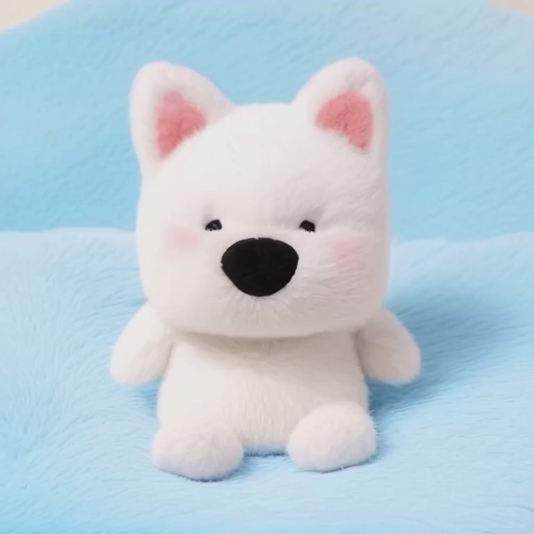 A short, static video of a small, white plush dog with pointed ears lined with pink. It has a large black nose and rosy cheeks, giving it a friendly and dependable look. The plushie is sitting on a soft, light-blue fluffy blanket.