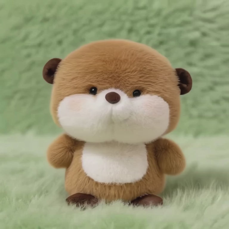 A short, static video showing a round, fluffy plush otter with light brown fur, chubby white cheeks, a white chest, and a cheerful expression. It is sitting on a soft, mint-green fluffy surface.