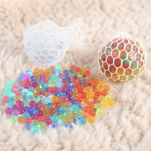 Colorful gel beads and a mesh bag on a beige surface