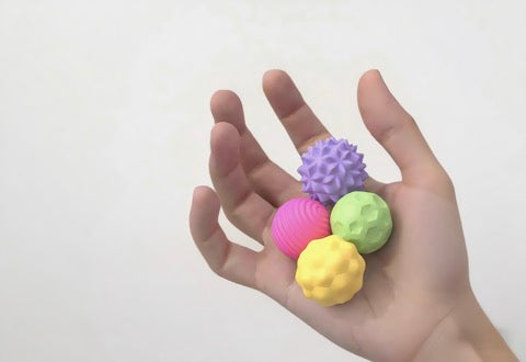 Hand holding three colorful textured balls against a white background