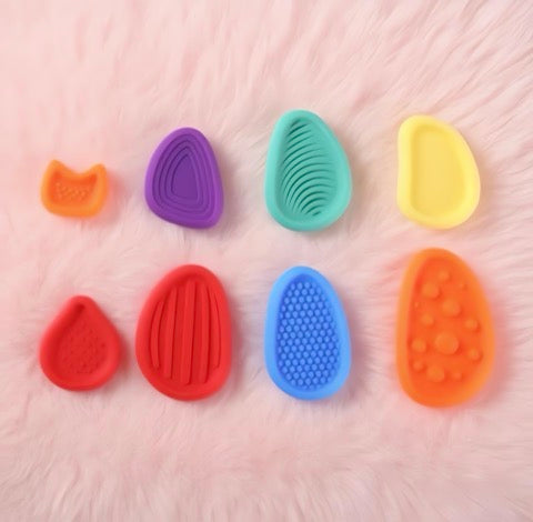 Set of colorful silicone pet grooming tools on a pink surface