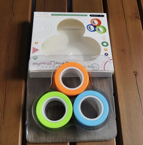 Four colorful fidget rings on a wooden surface with packaging in the background.