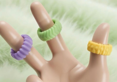 Three colorful rubber bands on a mannequin hand against a light green background