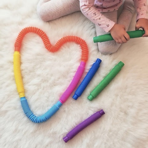 Colorful coiled tubes on a white surface with a child's legs in the background.