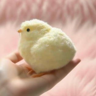 Small fluffy white toy chick held in a hand against a pink background