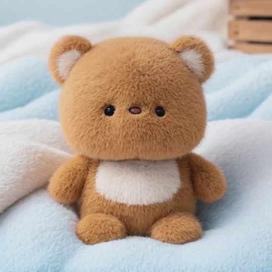 A short video of a fluffy, light brown teddy bear with a white chest patch, sitting on a blue and white blanket. The bear, called Brave Bear, raises its arms up and outwards in a big, welcoming gesture.